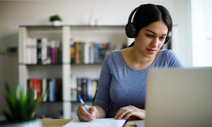 A woman at the computer, listening and taking notes