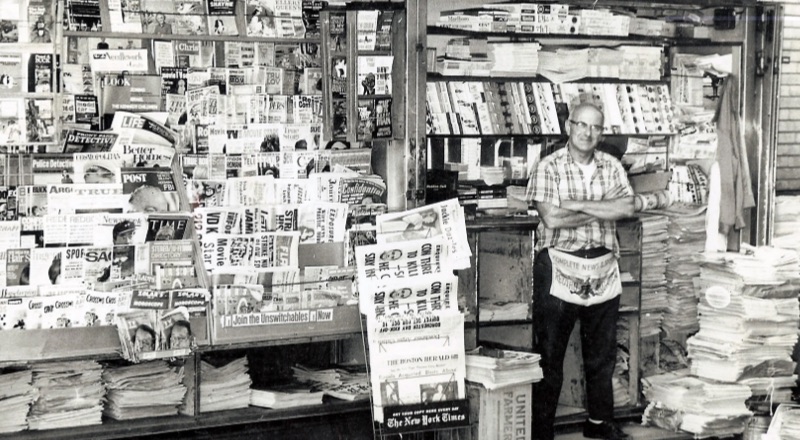 An old photo of a man standing in front of his newspaper stall