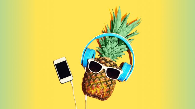 A pineapple listens to a podcast wearing headphones on a bright background.