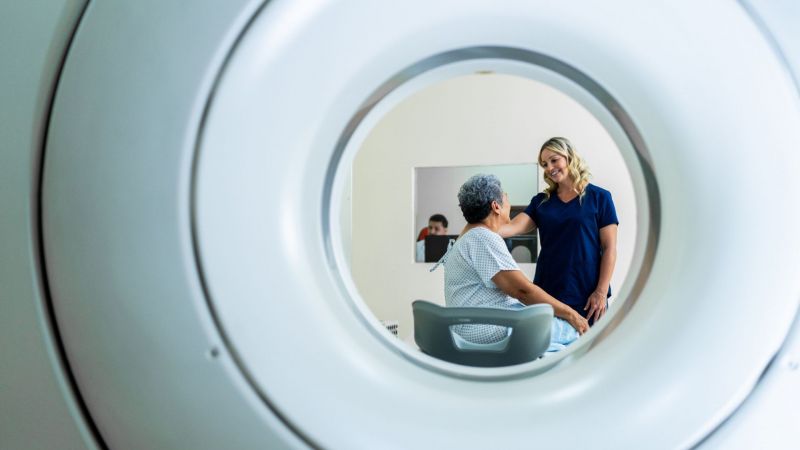 View though MRI machine of nurse talking to a patient. Human-centred care concept.