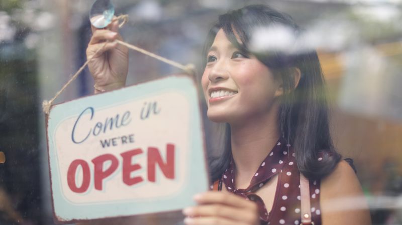 Happy business owner hanging an open sign at a cafe.