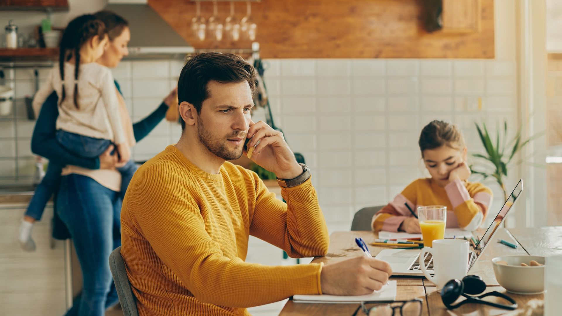 Adult man working from home working from home with his family is in the background.
