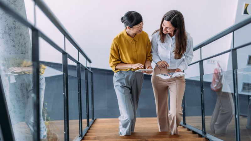 Two businesswomen walking up the stairs in a modern office.