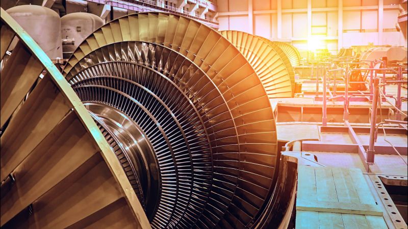 A close-up view of a large turbine blade inside a power plant, bathed in the warm light of the afternoon sun