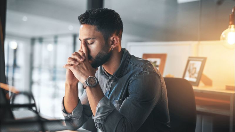 A young businessman holds his face while working in his office late at night