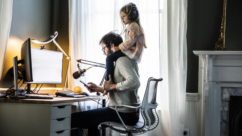 A man working from home office with a child sitting on his shoulders