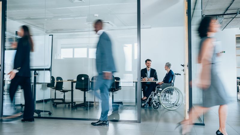 People walk through in the office, one person in a wheelchair