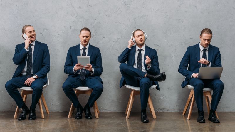 Four men in suits using digital devices, grey wall background
