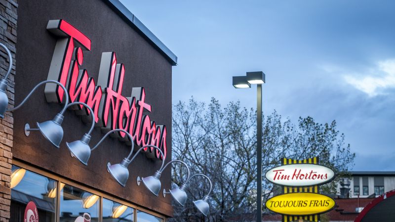 Tim Hortons logo in front of one of their restaurants in Quebec with their slogan in French in the background. 