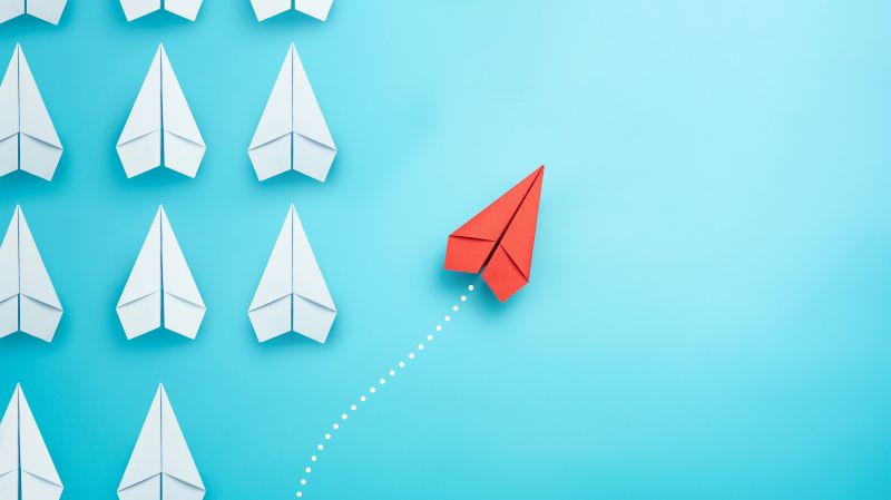 Group of white paper planes in one direction and one red paper plane pointing in different way 