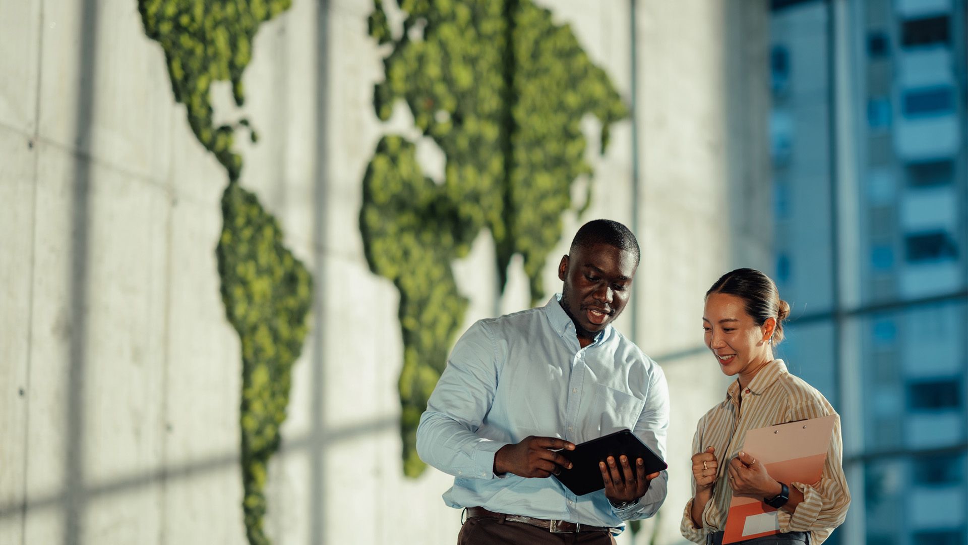 Two managers are discussing sustainable business strategies using digital tablet and clipboard, with a green world map in the background symbolizing global environmental awareness