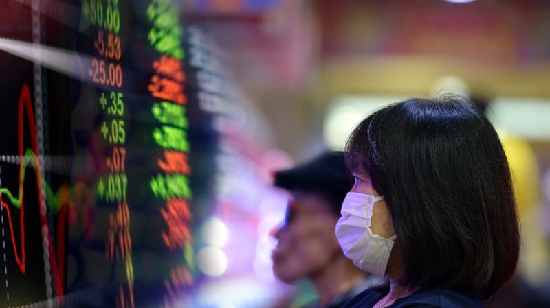 Local citizens with facemasks to protect them, looking at the red and green graphs of the stock market on a TV screen in Tokyo, Japan.