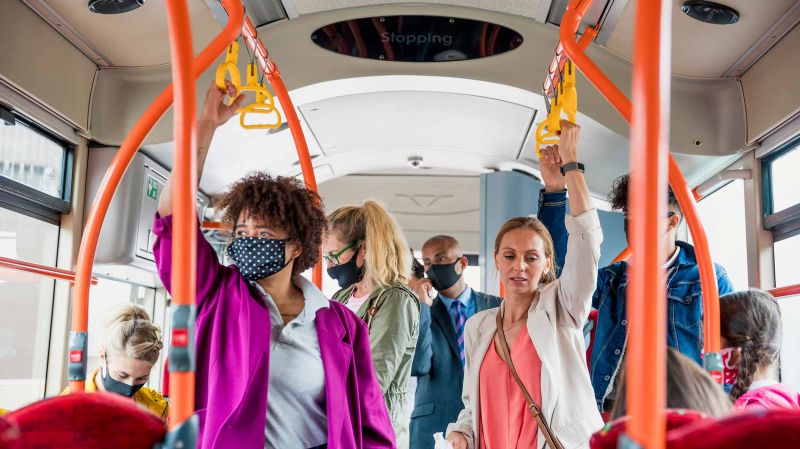 Passengers on a bus wearing protective masks during the COVID-19 pandemic. One woman is not wearing a mask.