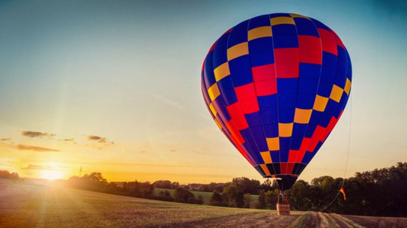 A hot air balloon sits in a field at sunrise