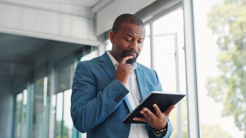 A man looking at information on a tablet and thoughtfully considering investment decisions.