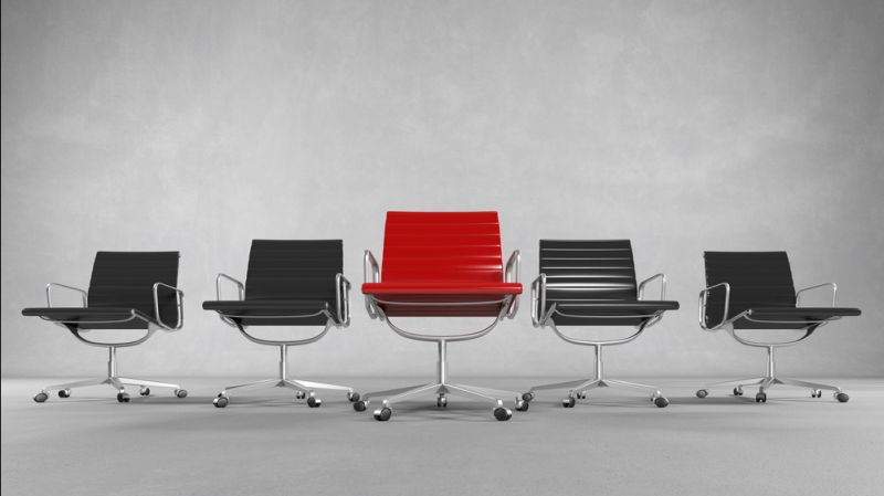 Red executive business chair surrounded by black chairs.