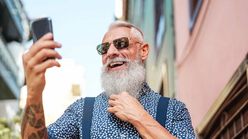 Hip bearded senior using a mobile phone outdoors.