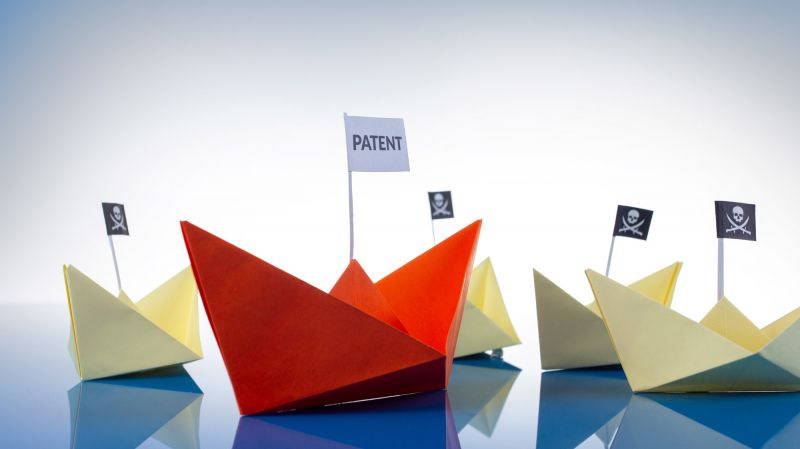 Intellectual property concept. Red paper boat with patent flag surrounded by white paper boats with pirate flags.