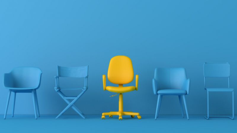 A yellow chair sits in the middle of a blue room with blue chairs beside it. 