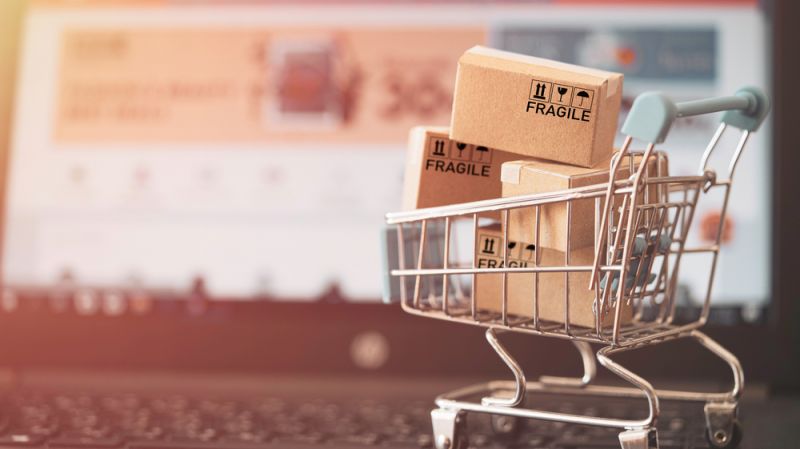 Small cardboard boxes in mini shopping cart on computer laptop.