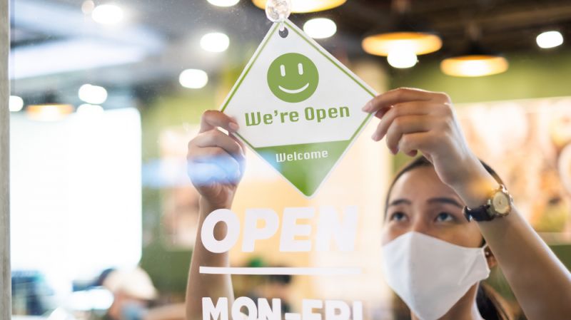 Business owner wear protective face mask while hanging an open sign at her restaurant.