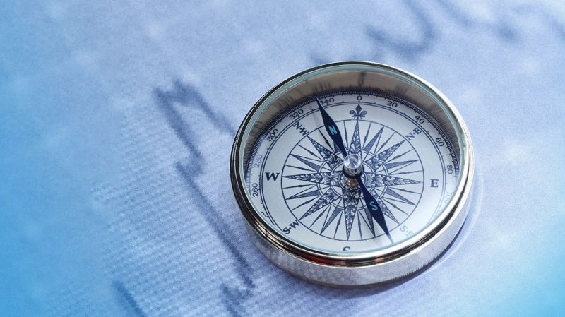 Close-up of a compass on stock market data chart.