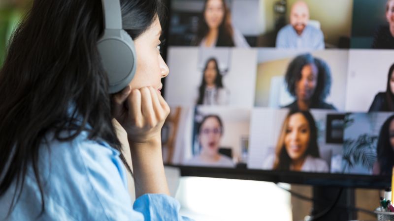 A corporate employee wearing headphones and resting her chin on her hand as she meets with her global virtual team on screen. 