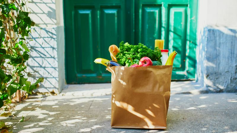 Bag of fresh produce and grocery items sitting on a doorstep in front of a green door.