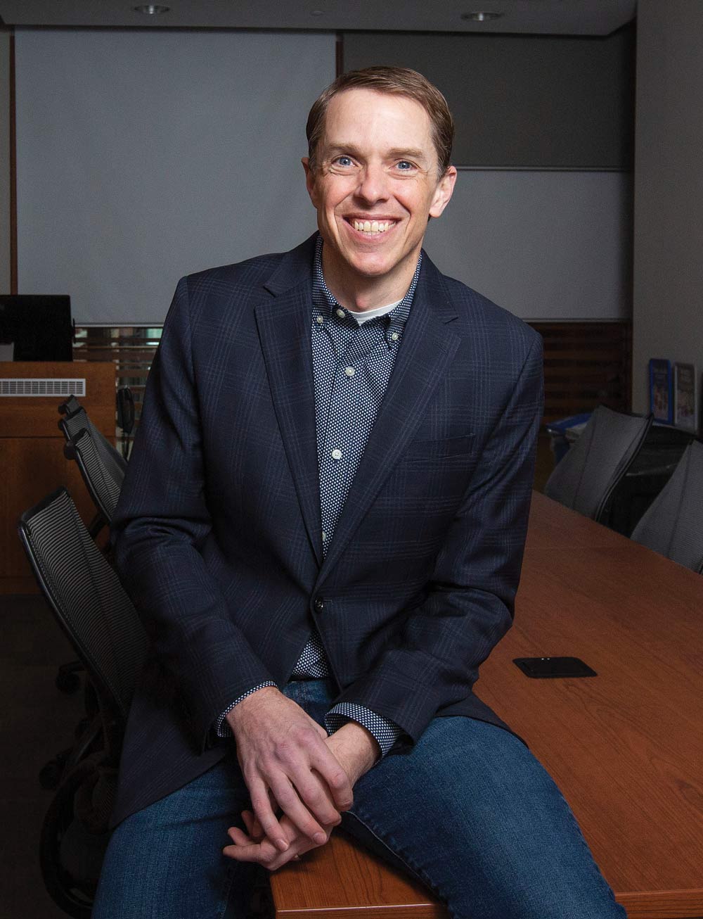 Jacob Brower stands beside the wall in a board room as he smiles wide for the camera. 